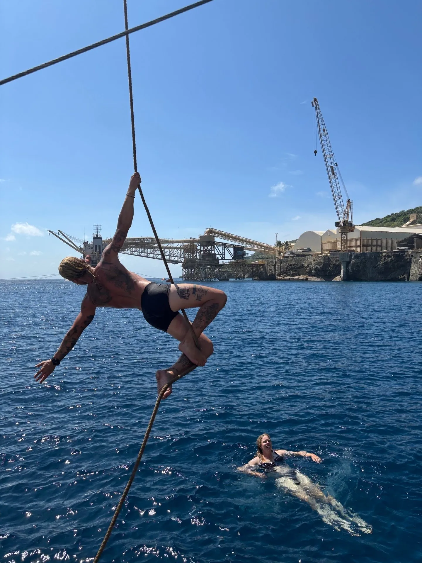 A crew member climbing a rope over the water off Christmas Island while another swims below